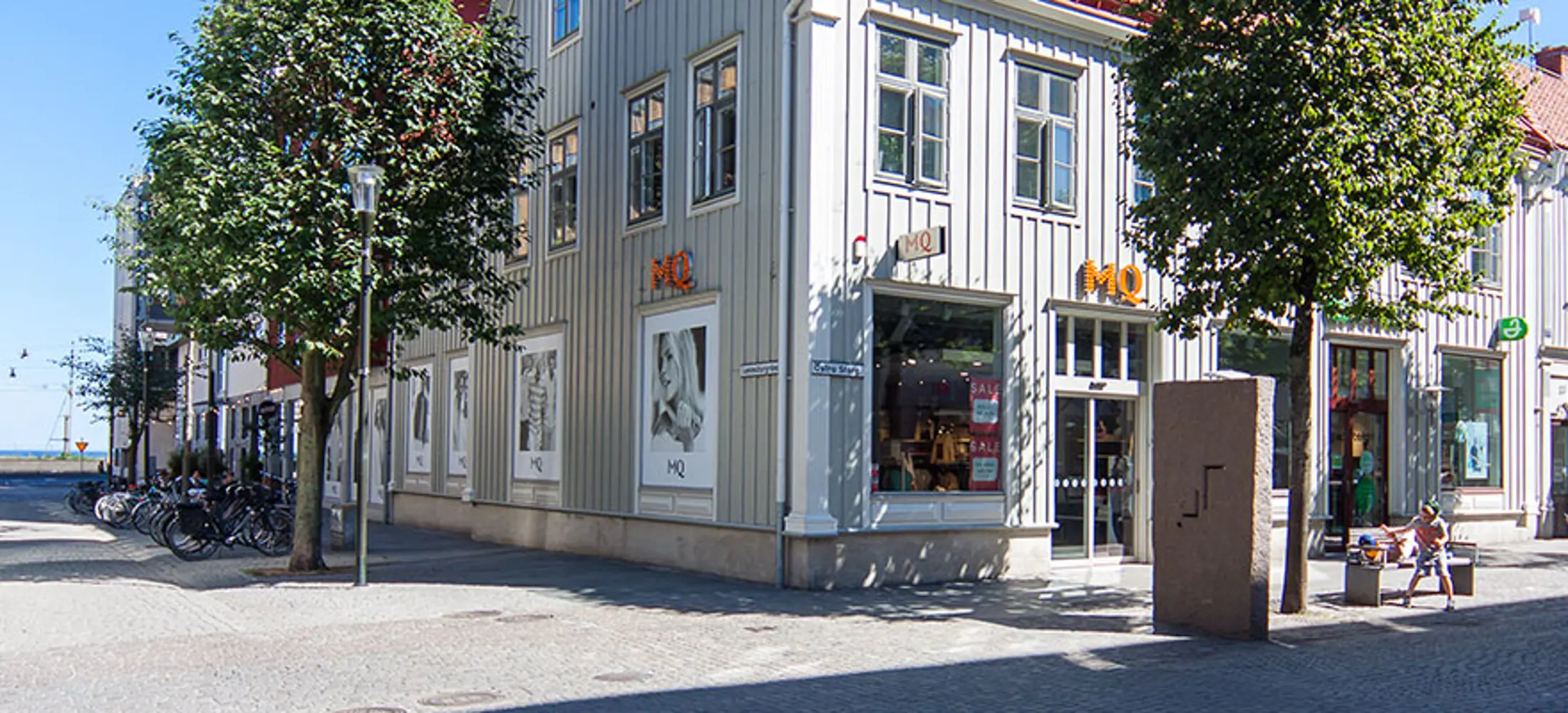 Handelsfastighet med en mintgrön träfasad, två träd framför byggnaden | Nivika Fastigheter AB (publ)