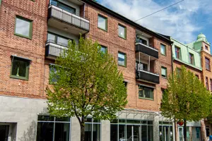Flerbostadshus med röd tegelfasad samt grå stenfasad, träd i förgrunden | Nivika Fastigheter AB (publ)