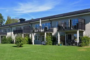 Flerbostadshus med ljusgrå fasad och vita fönster, svart tak, gräsmatta framför byggnaden | Nivika Fastigheter AB (publ)