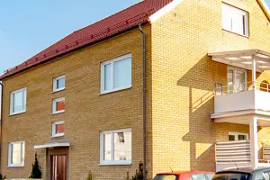 Flerbostadshus med gul tegelfasad, vita fönster och rött tegeltak | Nivika Fastigheter AB (publ)