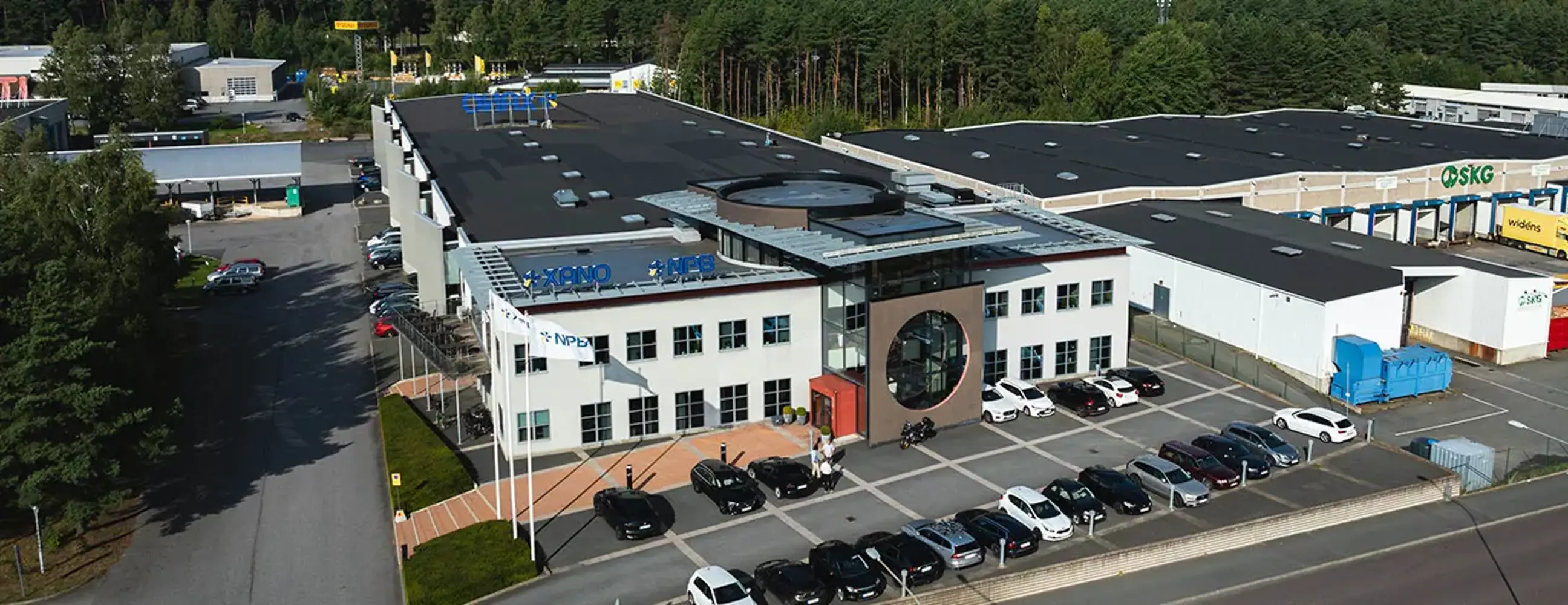 Industrifastighet med vit fasad och svart tak, parkering på framsidan | Nivika Fastigheter AB (publ)