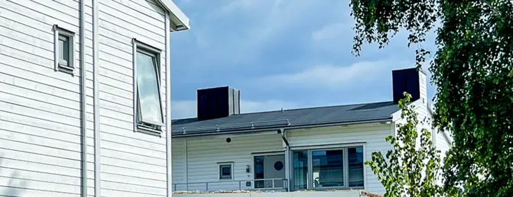 Bostadshus med vit träfasad, träd i förgrunden, närbild | Nivika Fastigheter AB (publ)